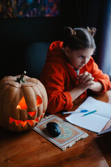 Caucasian happy girl orange color cloths near carved Halloween pumpkin studying online laptop