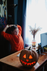 Caucasian happy girl orange color cloths near carved Halloween pumpkin studying online laptop