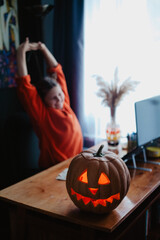 Caucasian happy girl orange color cloths near carved Halloween pumpkin studying online laptop
