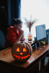 Caucasian happy girl orange color cloths near carved Halloween pumpkin studying online laptop