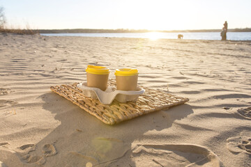 Pair of paper cups on a beach at sunset, ready for branding or design. Perfect for marketing materials, outdoor coffee themes, and customizable product placement in nature settings