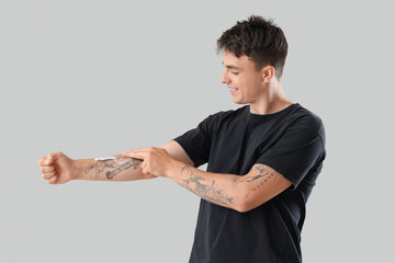 Young man applying cream on his tattooed arm against light background
