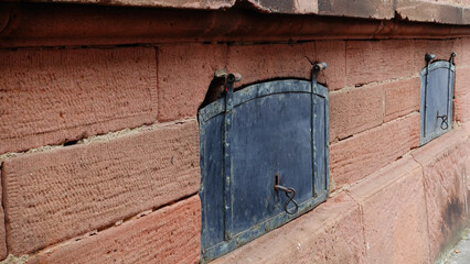 This structure features a weathered stone wall adorned with vintage iron doors set into the...