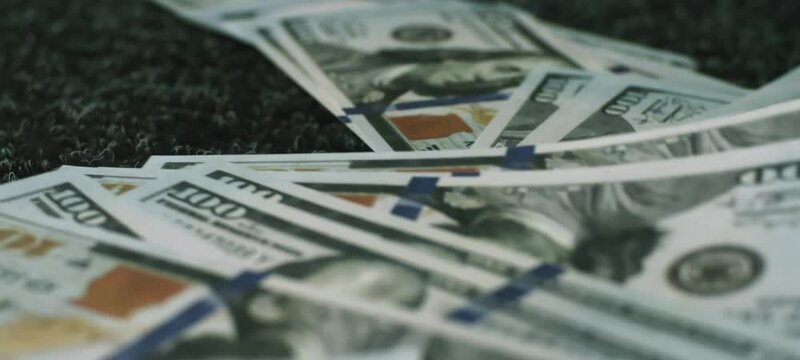 Extreme close-up view of a stack of one hundred dollar bills falling on a black table in slow-motion