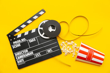 Movie clapper with film reels and popcorn on yellow background