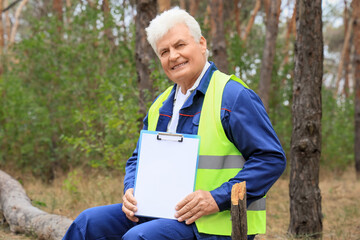 Senior forester with blank clipboard sitting on log in forest