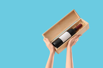Female hands holding box with bottle of wine on blue background