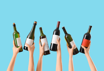 Female hands holding bottles of wine on blue background