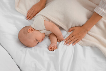 Mother covering her sleeping baby with soft blanket on bed, top view
