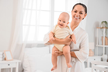 Happy mother holding her little baby in bedroom