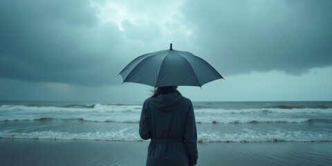 A person stands at the beach with an umbrella, gazing at the stormy ocean, evoking feelings of solitude and contemplation in a moody, atmospheric setting.
