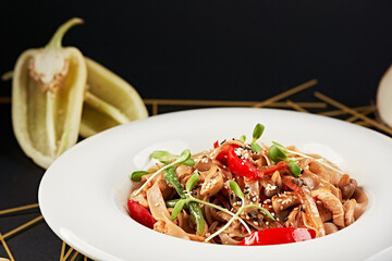 Plate with pasta, artistically presented on a black background framed by vegetables and flowers....