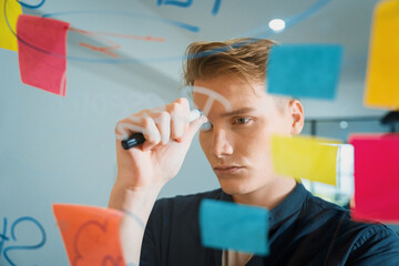 Professional caucasian businessman brainstorming marketing idea by using mind map and sticky notes on glass board at modern meeting room. Creative business and planing concept. Immaculate.