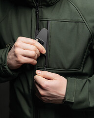 close-up photo of a man taking out a phone from his jacket pocket on a dark background under a lantern