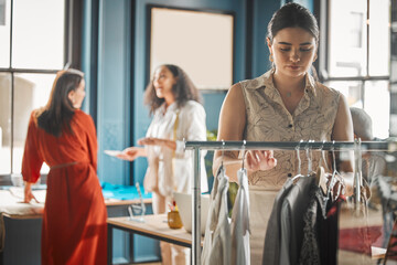 Obraz premium Fashion designer, woman and check clothes on rack for quality control, shop inspection or inventory. Tailor, clothing rail or fabric for retail stock, sales or choice for customer in startup boutique