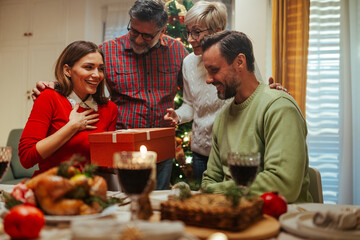 Family giving christmas present to surprised woman at dinner table