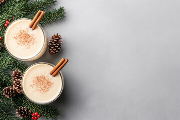 Fototapeta premium Two glasses of eggnog topped with cinnamon sticks and star anise. Evergreen sprigs in the background