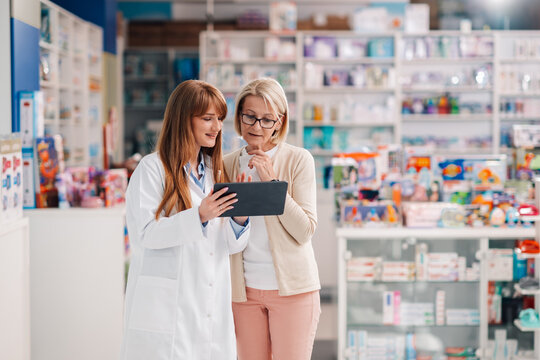 Pharmacist showing information on digital tablet to customer in drugstore