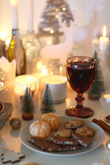 Various Christmas decorations, cookies, chocolate, nuts and tangerines, wine glasses and lit candles on the table. Holiday hygge at home. Selective focus.