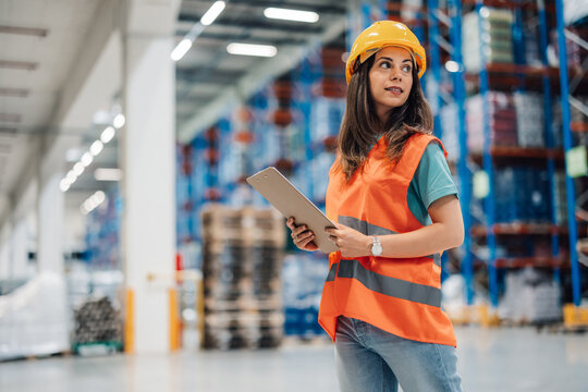 Female warehouse worker holding a clipboard checking inventory in a large warehouse