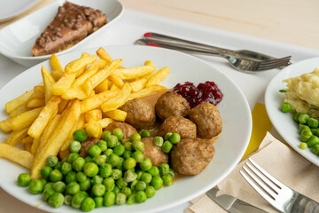 Meatballs with french fries, green peas, bechamel sauce and cranberry jam, meat balls on white plate