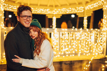 A festive loving couple is hugging on city street on christmas eve.