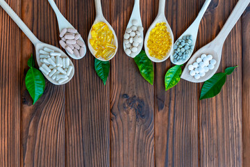 Variety of supplements on wooden spoons with green leaves. Wooden spoons are arranged in a row, each filled with different types of supplements. Top view. Free space for text.