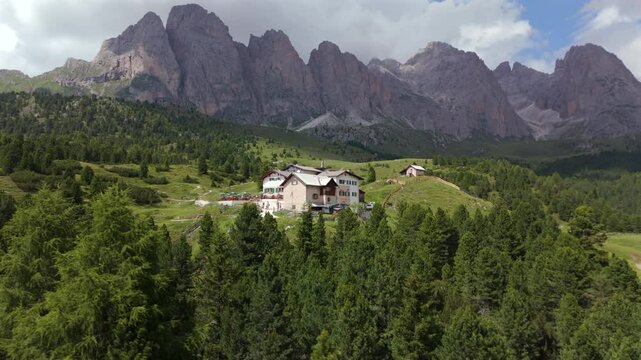 Aerial shots of Regensburger H&uuml;tte surrounded by dense alpine forests, with the dramatic peaks of Seceda towering in the background in the Dolomites.