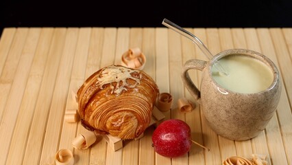 Ceramic mug filled with creamy vegetable beverage near croissant, autumn harvest setup emphasizing fresh produce, natural light, vibrant seasonal colors, rustic theme.