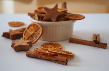 Auf einem Tisch steht ein weißes Förmchen, gefüllt mit verschiedenen Gewürzen, Orangenscheiben, Zimtstangen und Zimtherzen liegen daneben, Adventszeit