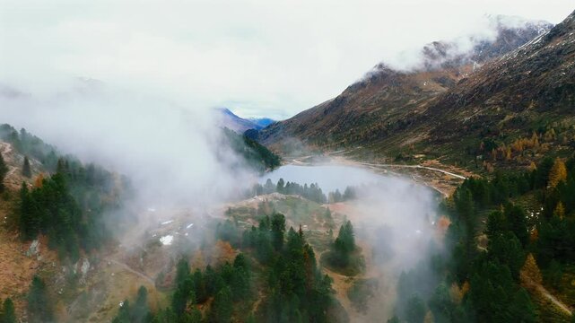 Aerial footage of clouds slowly covering the mountain peaks and descending into the alpine valley around Obersee Lake. The camera reveals the lake&rsquo;s reflective surface and surrounding highland forest.