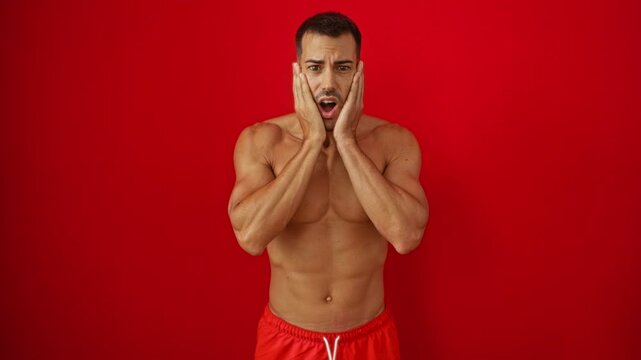 Young hispanic man shirtless in swimsuit with a surprised and amazed expression over isolated red background, shock and fear written on his face