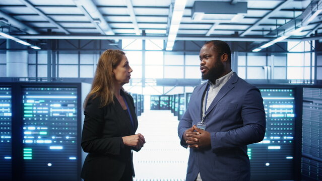 African american expert and coworker looking at holograms in data center, working together. Team members interacting with augmented reality AI visualization in server hub, camera B