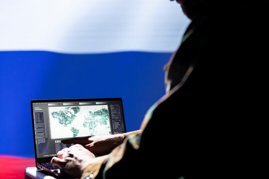 Russian ex KGB FSB operative engaged in surveillance mission using laptop, looking at world map. Intelligence officer isolated over Russia flag working for Kremlin regime monitoring zone of interest - Powered by Adobe