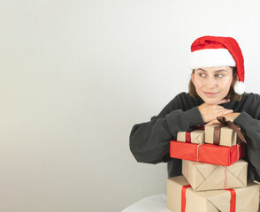 a woman in a Santa hat is thoughtfully standing near Christmas presents