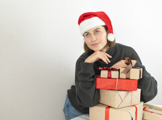 a woman in a Santa hat is thoughtfully standing near Christmas presents