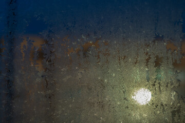 Frost-covered window with intricate ice crystals forming patterns, reflecting a soft light of sun from outside in a cold, winter scene.
