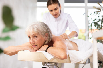 Portrait of elderly woman enjoying relaxing massage from professional female masseur in spa center..