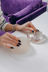 A woman chooses plastic breast implants at a doctor's consultation. The girl is holding silicone...