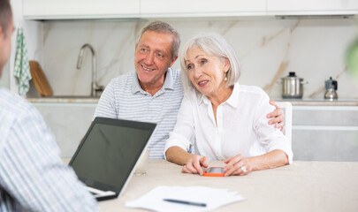Fototapeta premium Couple of elderly man and woman while discussing deal with male salesman in kitchen