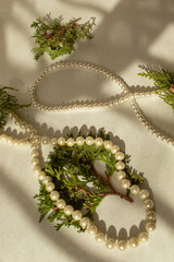 White pearls necklace and evergreen branch on textured background. Flat lay