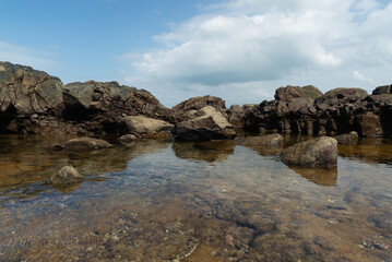 View of dark sea rocks against the ocean and cloudy sky. Preserved nature.
