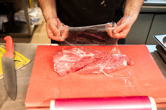 Chef preparing meat with plastic wrap in professional kitchen