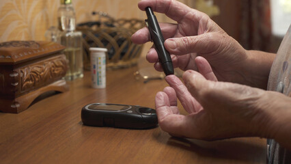 Old woman checking blood sugar levels at home. Hands close-up.