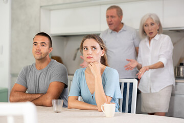 Portrait of an offended married couple in a home kitchen, which mature family members reprimand....