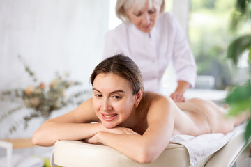 Obraz premium Portrait of young adult female client experiencing discomfort during back massage session in medical center. Painful massage concept..