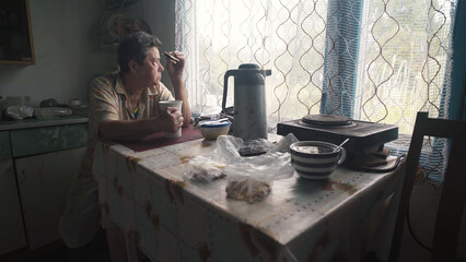 Elderly woman drinking tea in the kitchen of a poor village house.