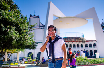 Young man talking on his smartphone, smiling during the call. People are seen walking around him.