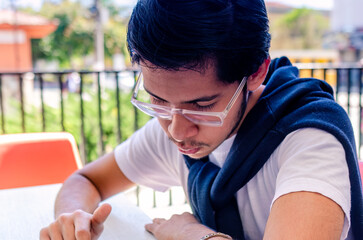 Close-up shot. Young Latino man stands in front of a table in a cafe, looking down where he...