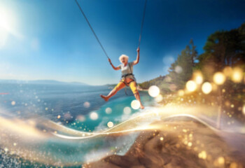 An elderly woman with white hair swings from a rope high above a lake with a mountain backdrop.